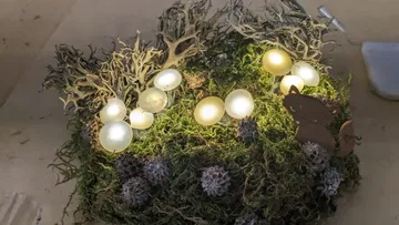 Glowing eggs lie on green moss with wooden figures.