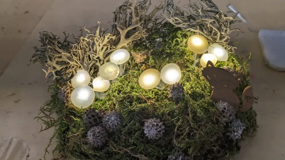 Glowing eggs lie on green moss with wooden figures.