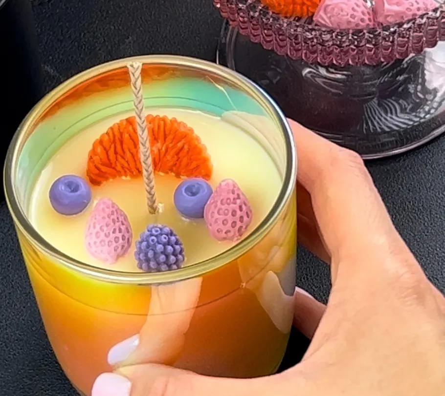 Bunte Kerze in Hand, gefüllt mit Kunstfrüchten.