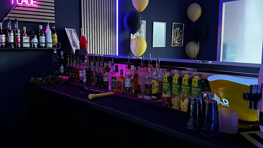 Bar counter with various liquor bottles and a neon sign.