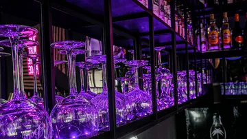 Glasses are placed on a shelf under purple lighting.