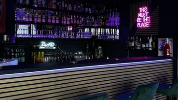 Wooden bar with neon lights, lots of liquor bottles behind it.