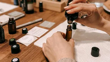A hand tips a bottle of essential oil onto a roll-on.