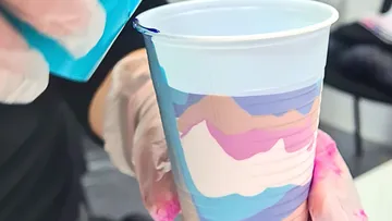 Bunte, fließende Kunst im Plastikbecher mit Handschuhen