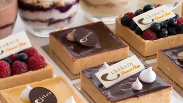 Torten mit Schokoladenglasur liegen neben Fruchtbechern.