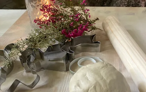 Cookie cutters, dough, rolling pin and flowers on table.