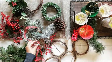 Hand arranging holiday wreath materials on table.