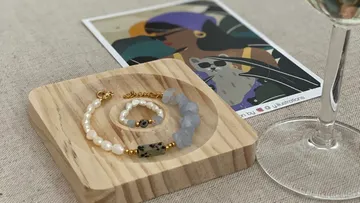 Schmuckstücke liegen auf einem Holzbrett neben einem Glas.