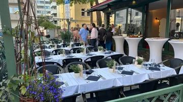 Tische sind gedeckt; Gäste unterhalten sich im Freien.