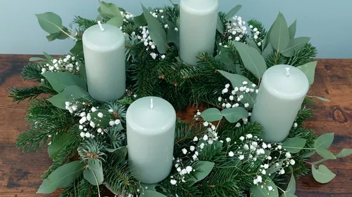 Grüne Kerzen auf einem mit Tannenzweigen geschmückten Kranz.