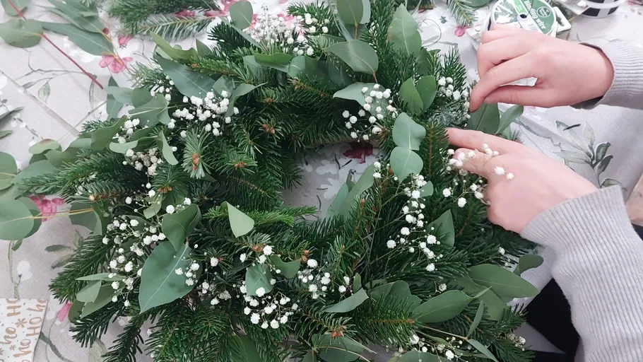 Kranz aus Tannenzweigen wird mit Blumen verziert.