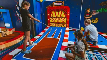 A girl is playing mini golf in a colorful playroom.