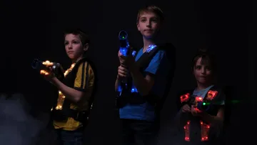Three children with glowing lasers in a dark environment.