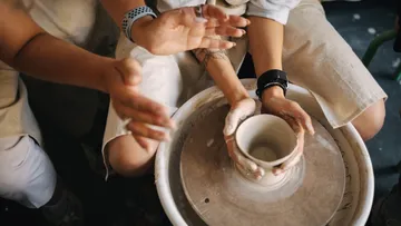 Hands shaping clay pot on pottery wheel.