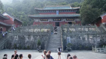 Old temple with visitors, surrounded by mountains and plants.