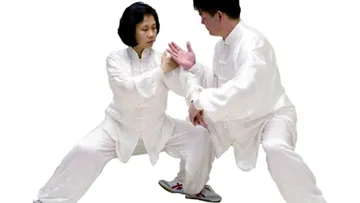Two people practice tai chi wearing white clothes.