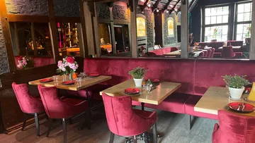 Rote Polsterstühle stehen an hellen Holztischen in Restaurant.
