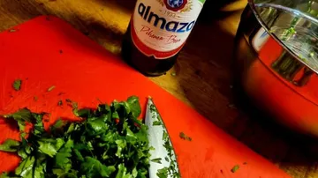 Gehackter Koriander liegt neben einer Flasche Bier auf Brett.