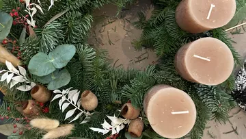 A wreath decorated with candles and green plants.