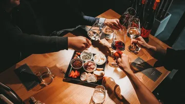 Table with drinks and snacks; people toast.