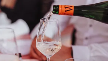 A bottle pours wine into a wine glass.