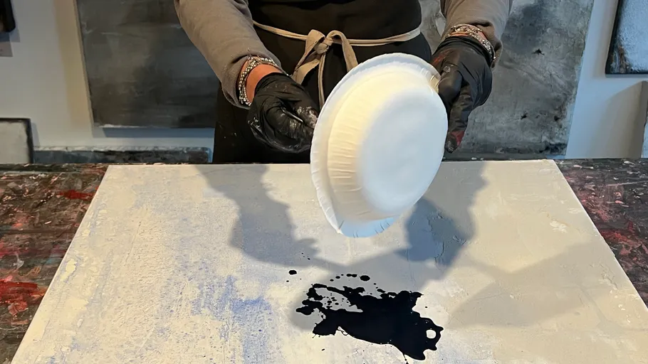 White plate tips black paint onto gray canvas.