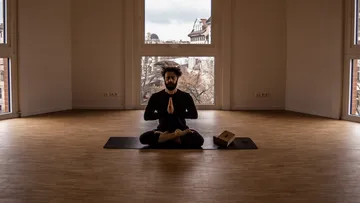 Man meditates in yoga style in an empty room.