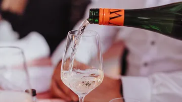 A bottle pours sparkling wine into a glass at the table.