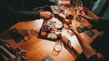 Tisch mit Snacks, Gläsern und anstoßenden Händen.