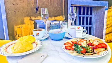 Frühstückstisch mit Croissants, Crepes und Getränken in lebhaftem Raum.