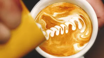 Kaffeetasse mit gemustertem Milchschaum in goldbraunem Getränk.
