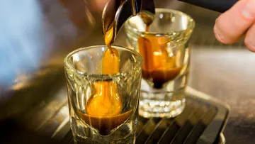 Espressomaschine gießt Kaffee in Gläser auf einer Theke.
