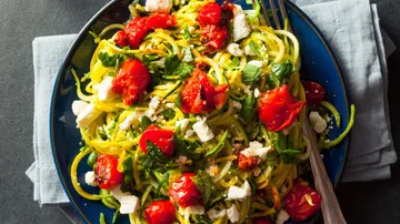 Zucchini noodles with tomatoes and feta cheese on a blue plate.