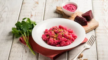 Red pasta on white plate with herbs and turnips.