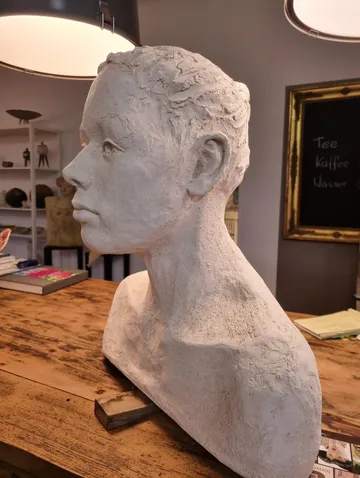 Skulptur eines Kopfes, steht auf einem Tisch, beleuchtet.