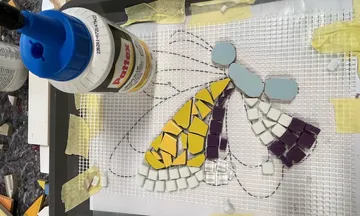 A mosaic is placed on a grid using glue.