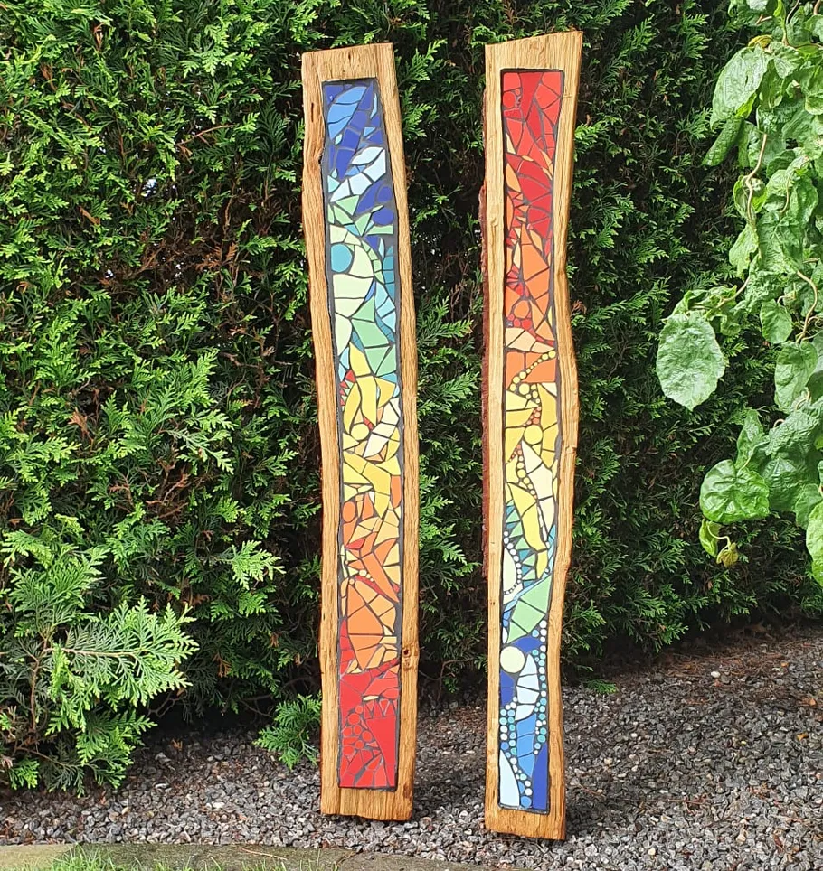 Bunte Mosaikplatten liegen auf Holz, umgeben von Pflanzen.