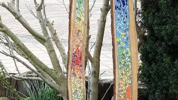 Bunte Mosaikwände hängen zwischen Bäumen im Garten.
