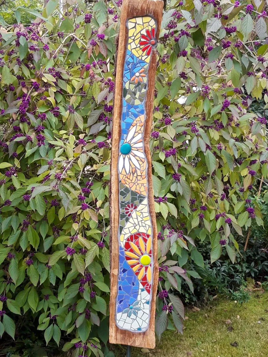 Bunte Mosaikplatte zeigt Blumenmuster zwischen grünen Blättern.