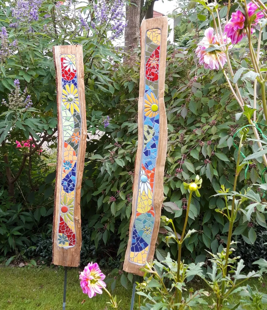 Zwei Holzleisten mit buntem Mosaik, umgeben von Pflanzen.