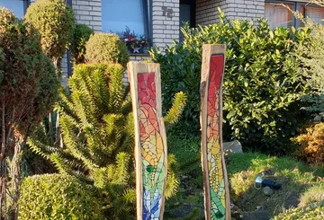Zwei farbige Holzsäulen stehen im Garten vor einem Haus.