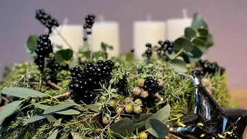 Kränze mit schwarzen Beeren, Kerzen und grünem Laub dekoriert.