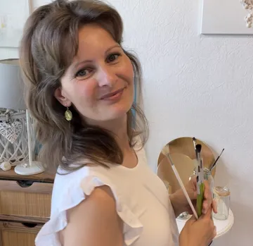 Woman holding paintbrushes, smiling, in art studio.