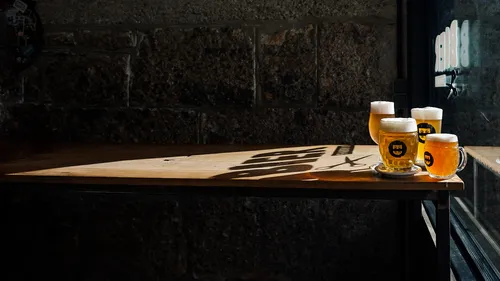 Glasses of beer stand on a wooden table, shadows visible.