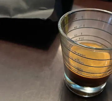 A measuring cup of freshly brewed espresso on a table.