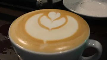 Tasse Kaffee mit kunstvoller Schaumdekoration auf Tablett.