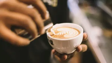 A hand pours milk into a coffee mug with a pattern.