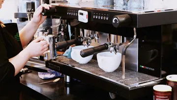 Barista froths milk on an espresso machine in a café.