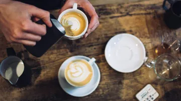 Tasse wird mit milchschaum dekoriert auf Holztisch.