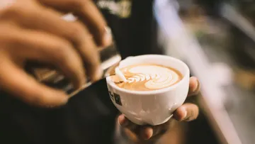 Eine Tasse Kaffee wird mit Milch verziert, hinterher.